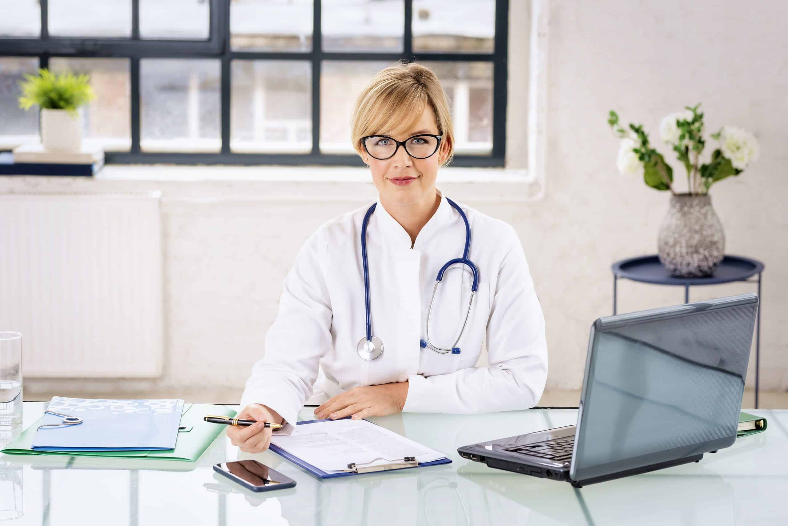 Smiling female healthcare worker using laptop and working in doctorâs room.