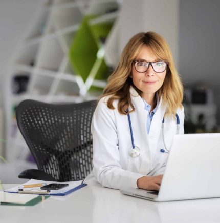 Smiling female healthcare worker using laptop and working in doctorâs room.